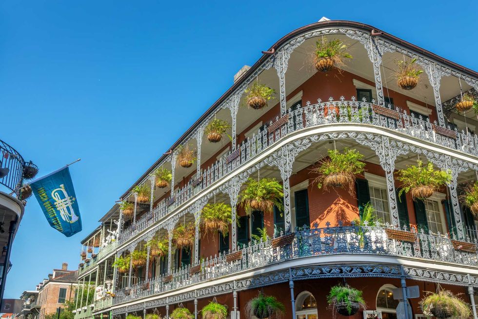 Ornate ironwork balconies with hanging plants in New Orleans, under a clear blue sky.