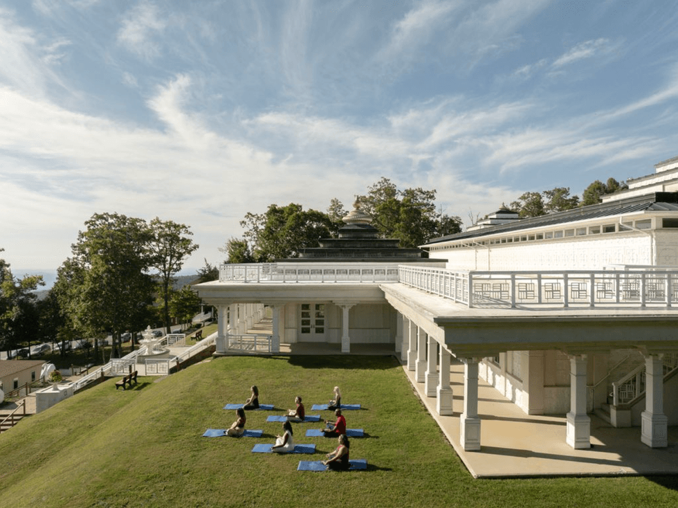 Outdoor yoga class on a grassy hill beside a large white building under a blue sky.