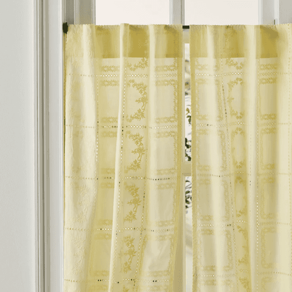 Pale yellow curtain with floral patterns hanging by a window.