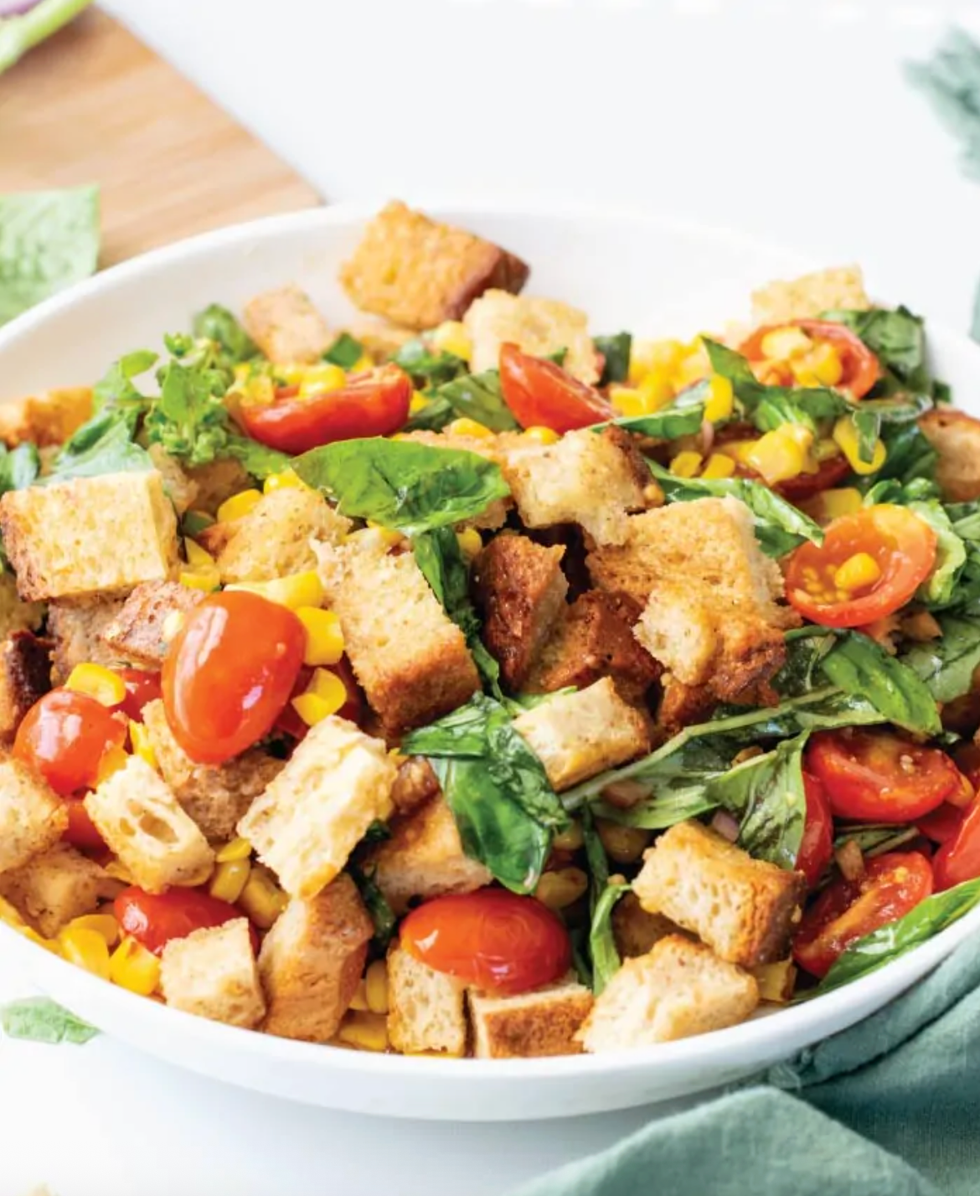 Panzanella salad with croutons, cherry tomatoes, corn, and lettuce in a white bowl.