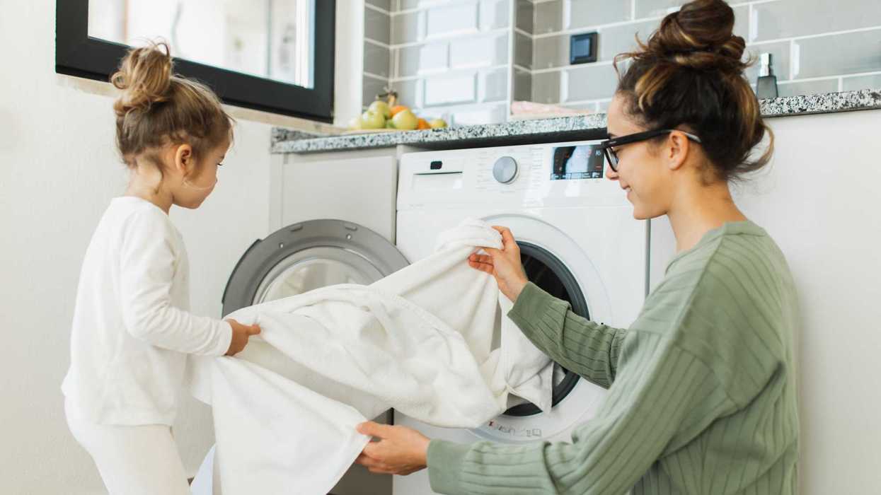 Parent and child doing laundry together in a modern kitchen.