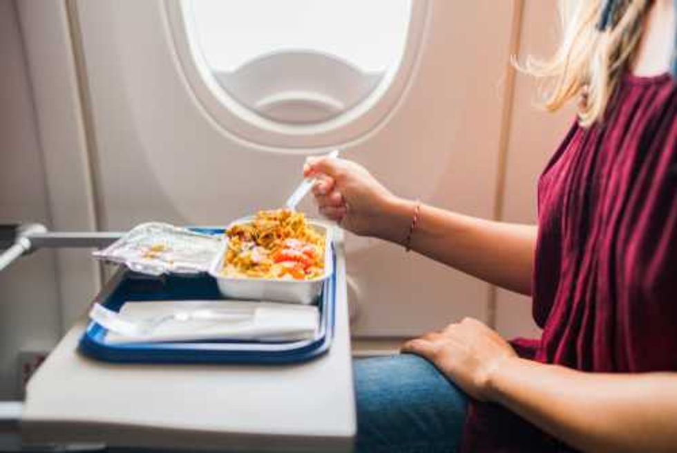 Passenger eating a meal on an airplane, tray table with a plastic fork and container.