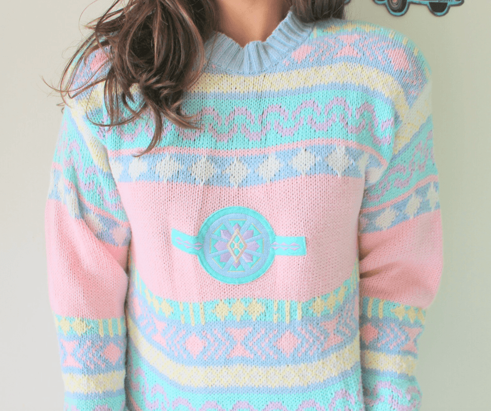 Pastel patterned sweater with geometric shapes and decorative emblem.