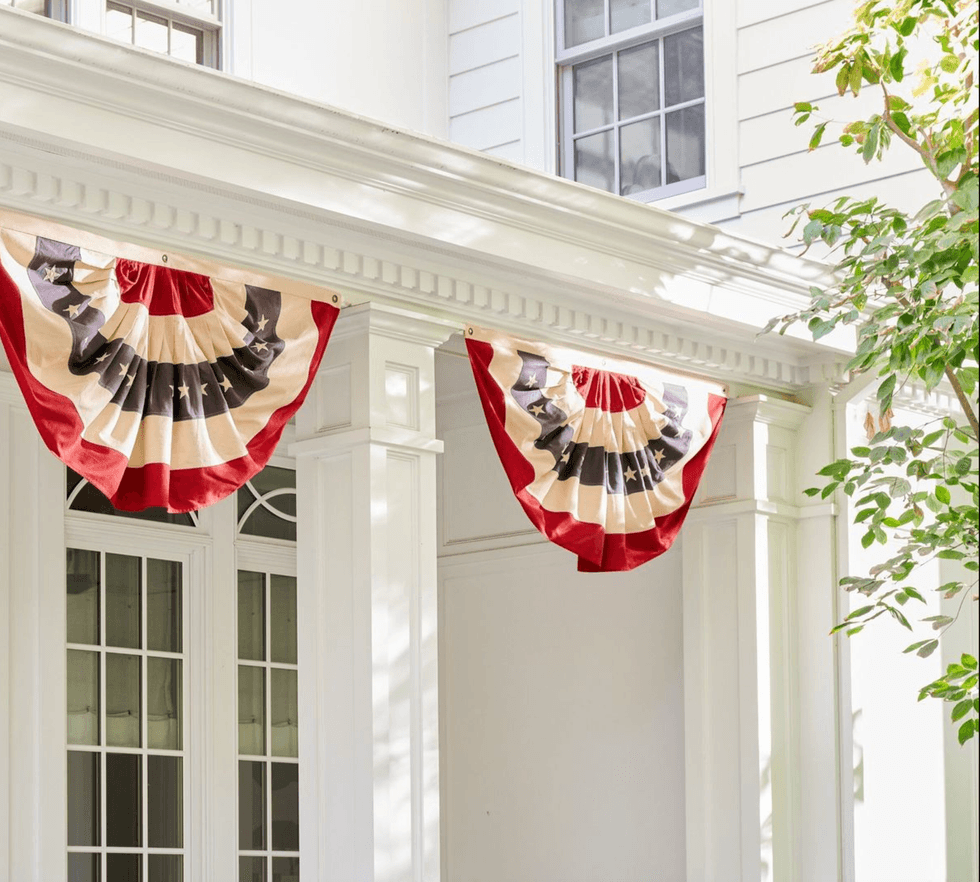 Patriotic bunting on a white house porch, with greenery on the side.