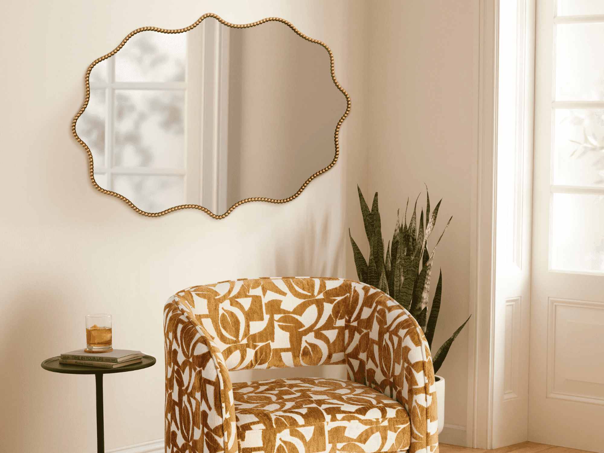 Patterned chair, scalloped mirror, and plant in sunlit room with small round table.