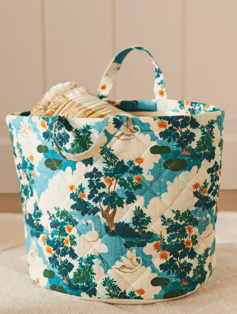 Patterned fabric basket with handles, holding beige knitted blankets.