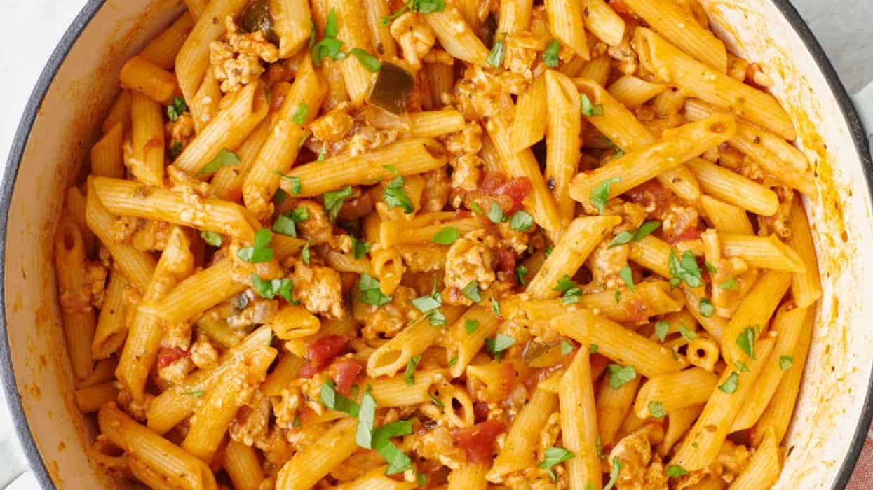 Penne pasta with tomato sauce and herbs, cooked in a pot, garnished with fresh basil.