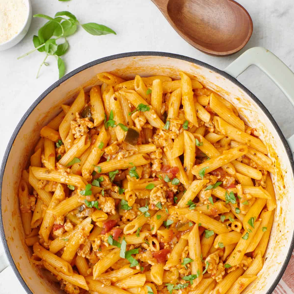 Penne pasta with tomato sauce and herbs, cooked in a pot, garnished with fresh basil.