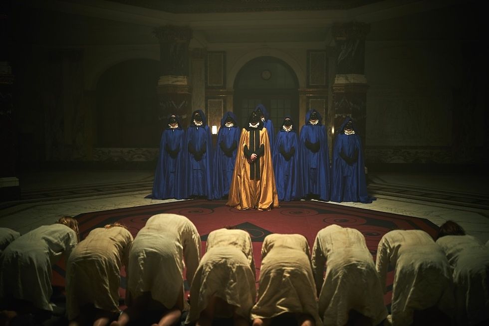 People bowing before masked figures in blue and gold robes in a dimly lit room.