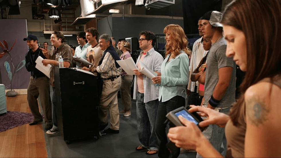 People gathered on a set, holding scripts, with a woman using a touchscreen device.