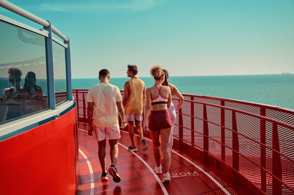 People jogging on a red track overlooking the ocean under a clear sky.