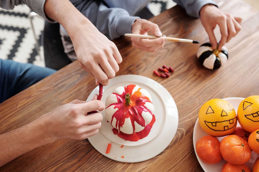 People painting pumpkins at a table with oranges decorated as jack-o'-lanterns.