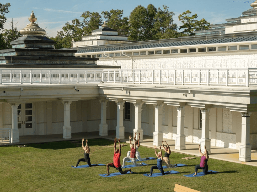 People practicing yoga on mats in a sunny courtyard near a white building with columns.