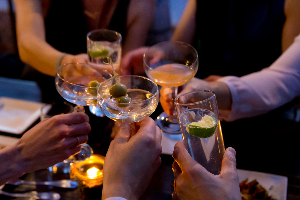 People toasting with cocktails and drinks at a dimly lit gathering.