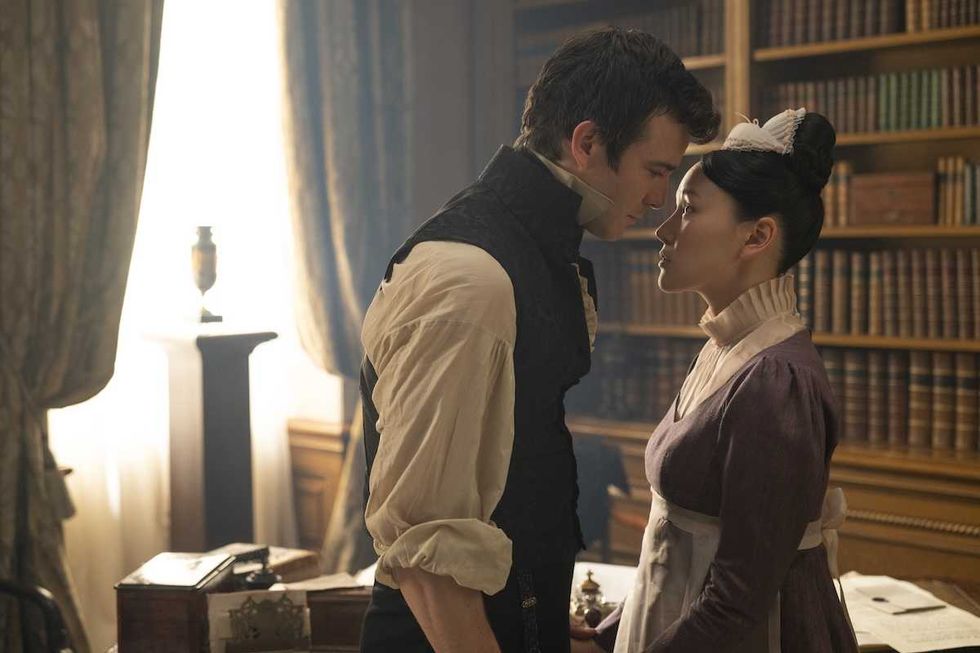 Period drama scene: a man and woman face each other closely in a library.
