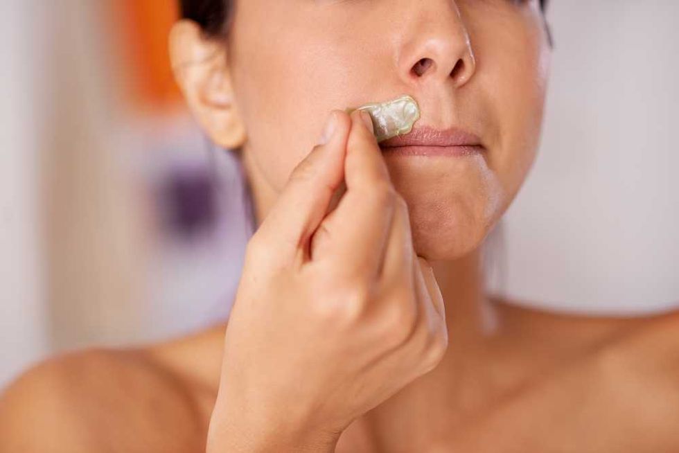 Person applying wax strip to upper lip for hair removal.