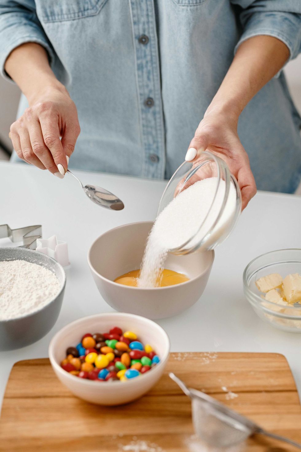 Person baking: pouring sugar into bowl, surrounded by ingredients.