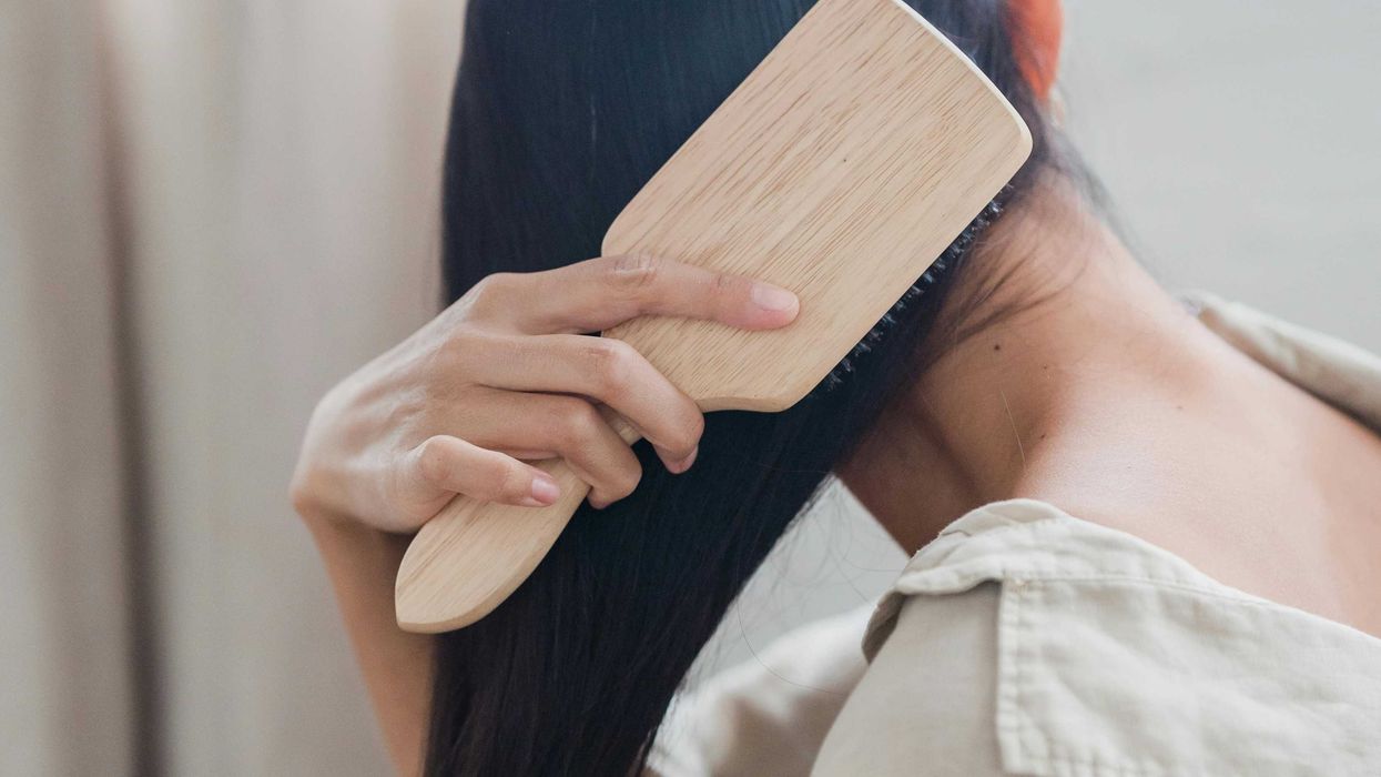 Person brushing long hair with a wooden brush, wearing a beige shirt.