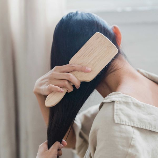 Person brushing long hair with a wooden brush, wearing a beige shirt.
