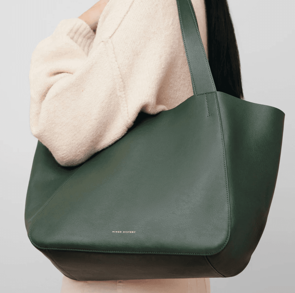 Person carrying a large dark green tote bag and wearing a cream sweater.