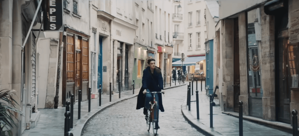 Person cycling on a narrow cobblestone street lined with shops and cafes.
