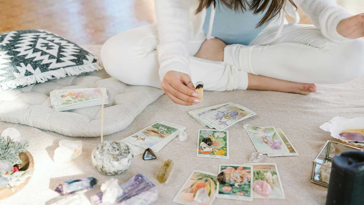 Person doing a tarot reading with crystals and incense on a mat.