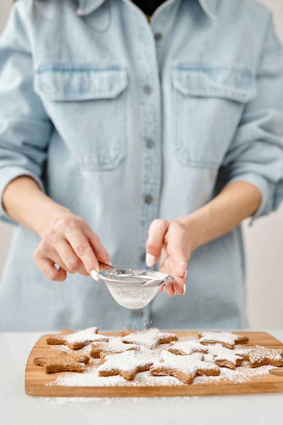 Person dusting powdered sugar on star-shaped cookies.