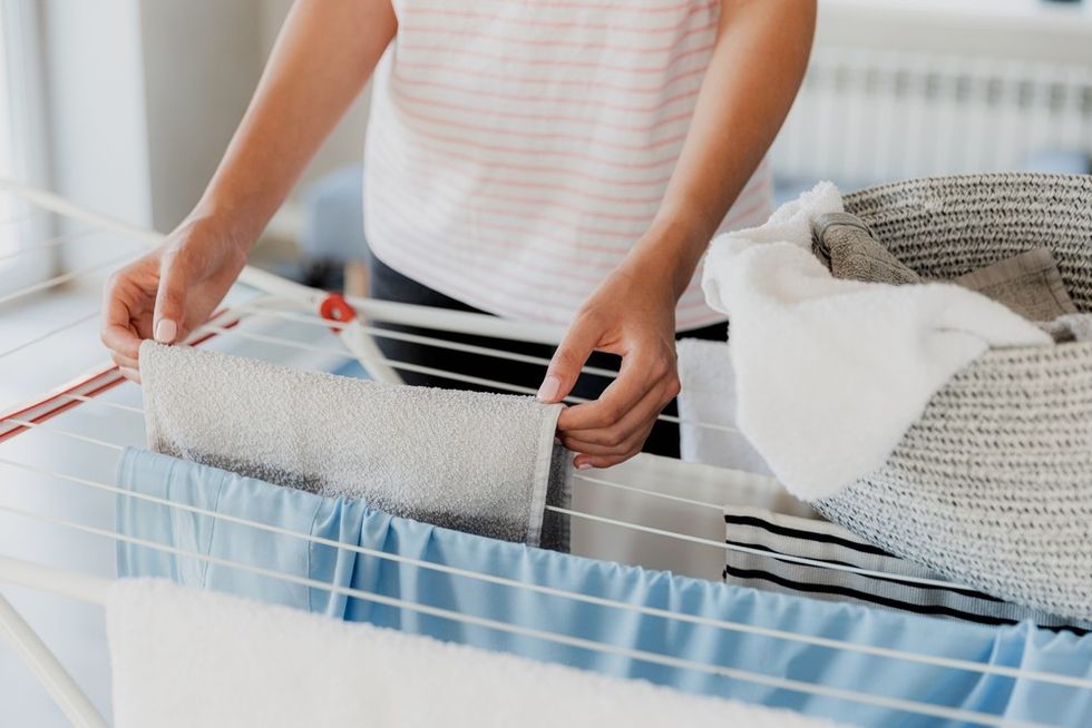 Person hanging a towel on a clothes drying rack next to a basket of laundry.