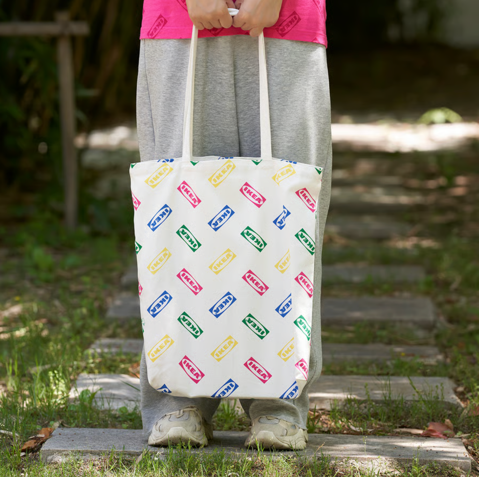 Person holding a colorful IKEA tote bag while standing on a garden path.