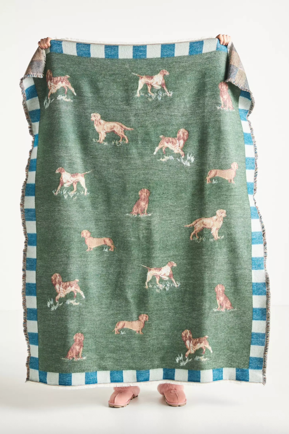 Person holding a dog-patterned blanket with pink slippers visible below.