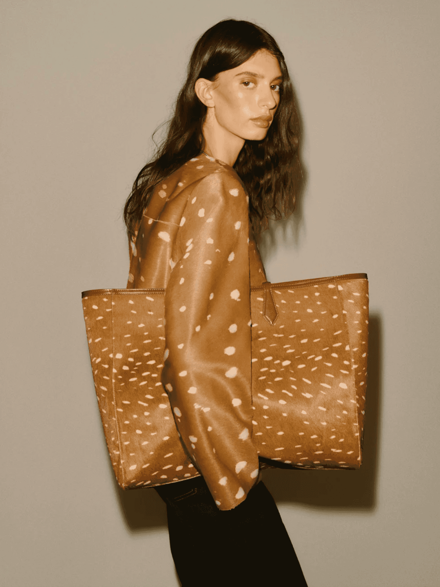 Person holding a large brown tote bag in a matching spotted jacket.