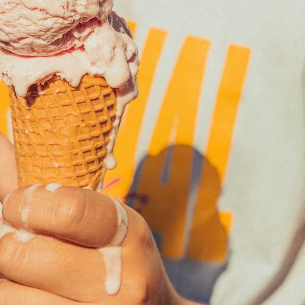 Person holding a melting ice cream cone, wearing a white T-shirt with yellow design.