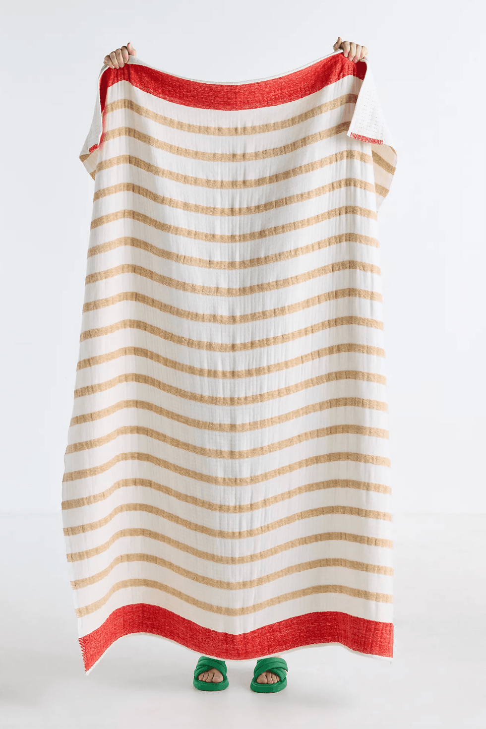 Person holding a striped blanket, red edges, green sandals visible below.