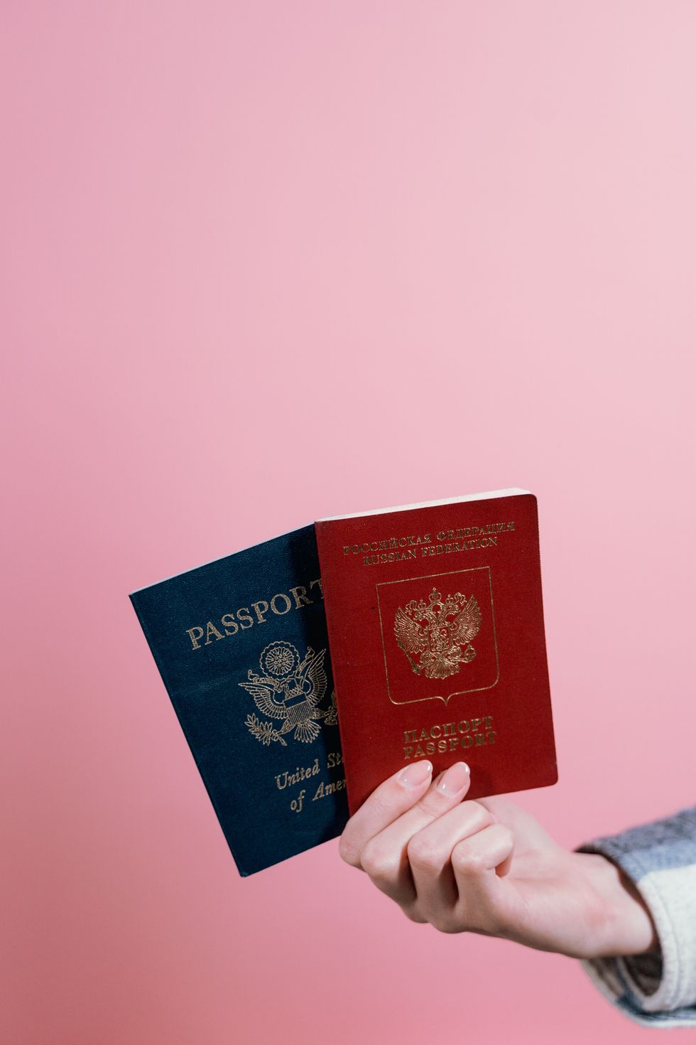 person holding two passports against pink background