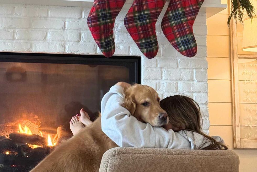 Person hugging dog by a fireplace, with stockings hanging above.