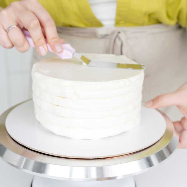 Person icing a white cake on a rotating stand with an offset spatula.