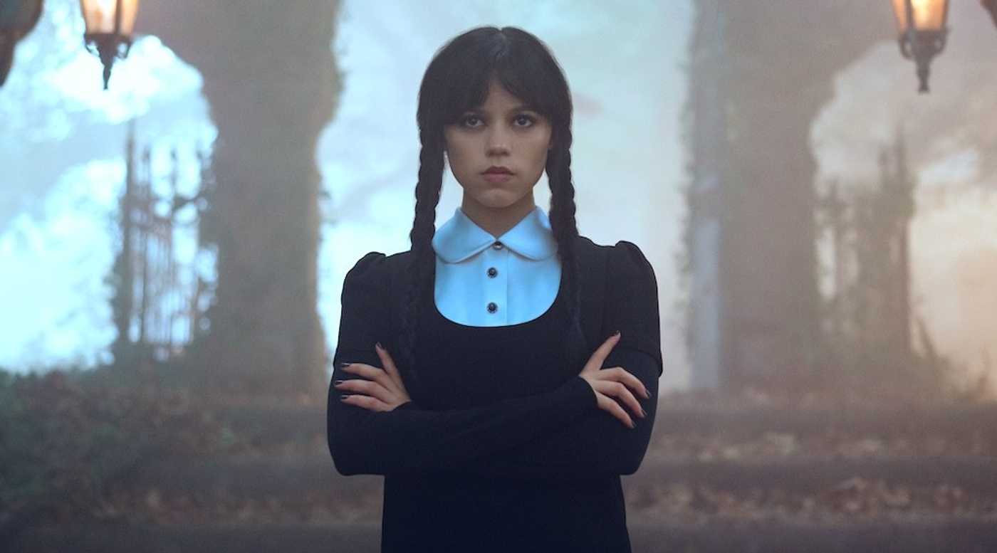 Person in a black dress and braids stands in a misty, autumnal forest with crossed arms wednesday season 3 release date