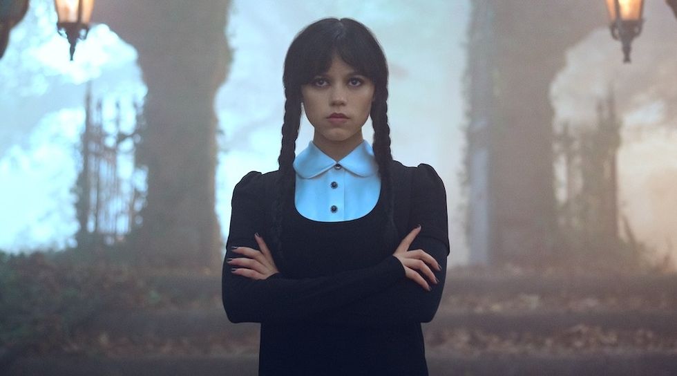 Person in a black dress and braids stands in a misty, autumnal forest with crossed arms wednesday season 3 release date