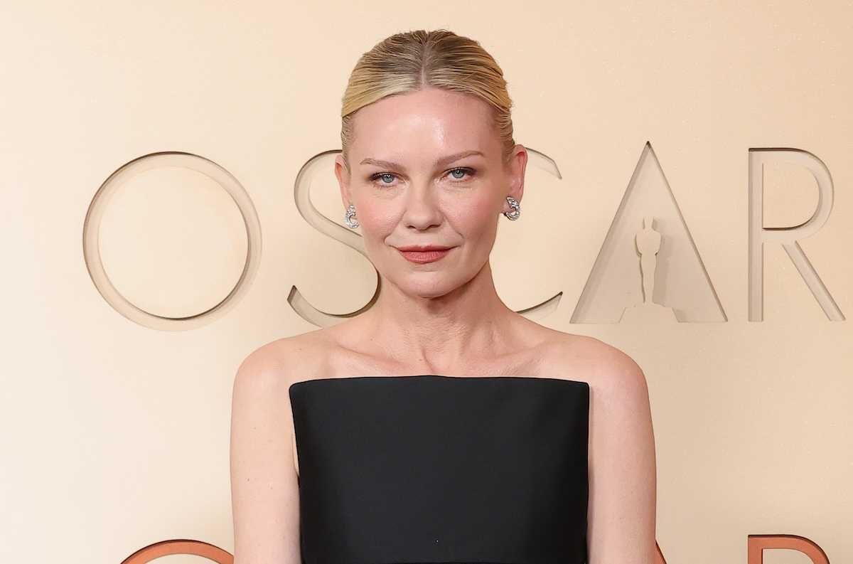 Person in a black dress, standing in front of an "Oscars" sign backdrop.