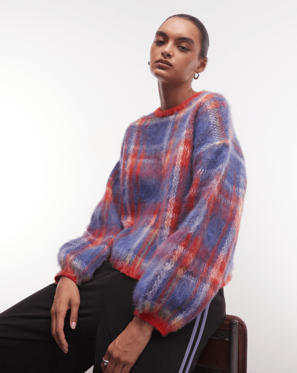 Person in a colorful, fluffy plaid sweater, seated against a plain background.