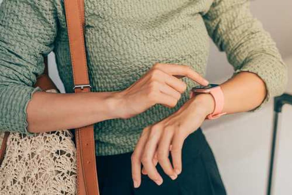 Person in a green top using a smartwatch, holding a woven bag.