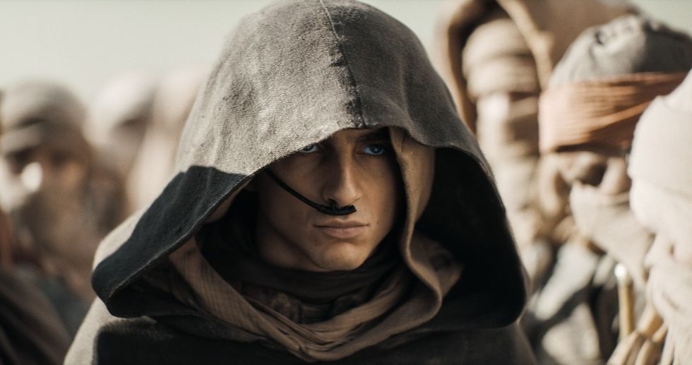Person in a hooded cloak with blue eyes, among others, wearing a survival device on their nose.