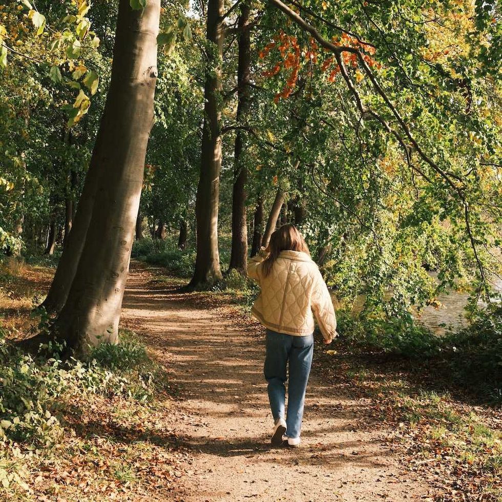 Person in a jacket walking on a leafy forest path.
