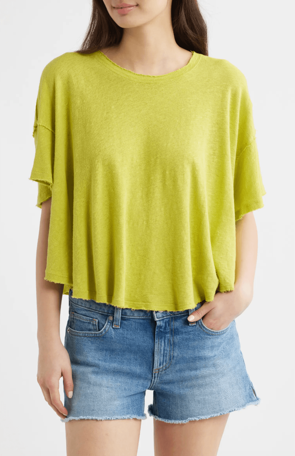 Person in a lime green loose top and denim shorts, hand in pocket.