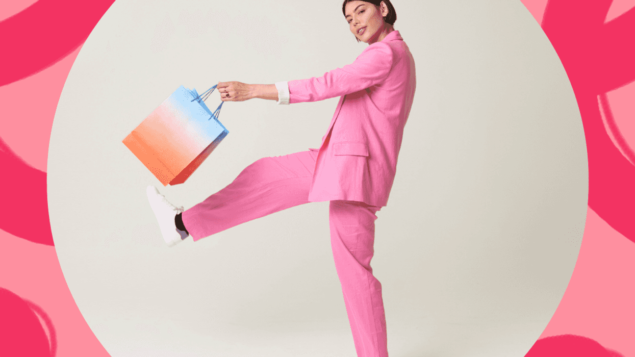 Person in a pink suit holding a colorful shopping bag, posing playfully on a pink background.