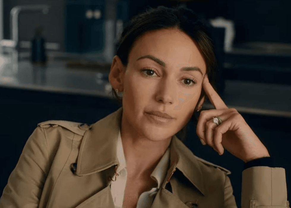 Person in a trench coat, resting chin on hand, looking thoughtfully to the side.