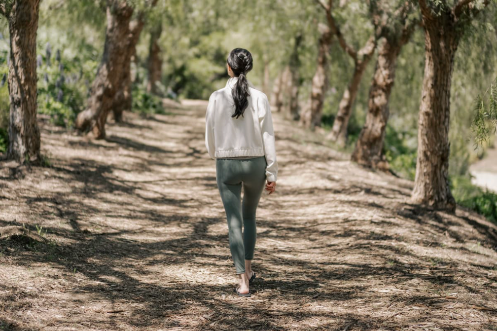 Person in activewear walking on a tree-lined path in a sunny forest.