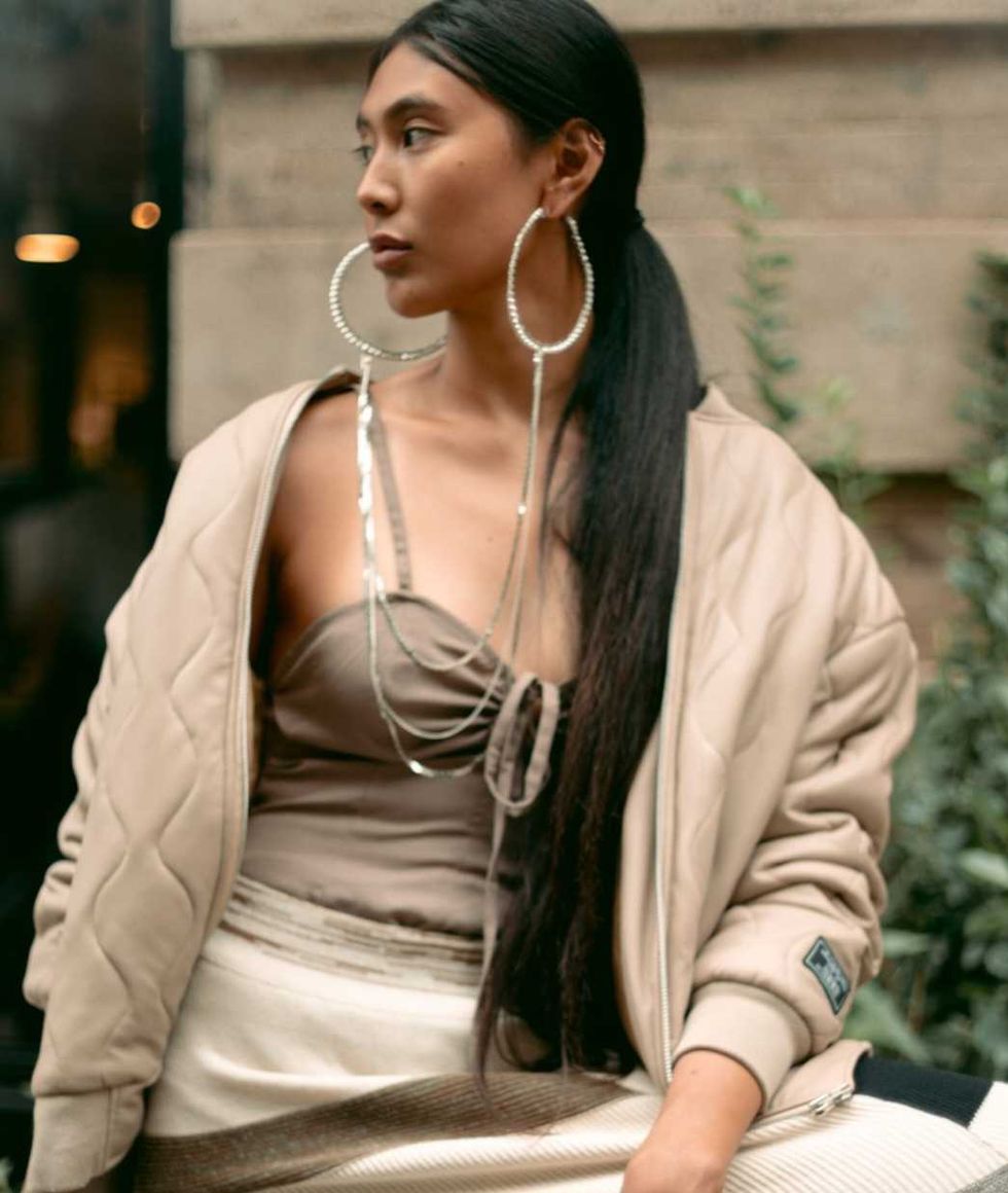 Person in beige outfit with large hoop earrings, looking to the side outdoors.