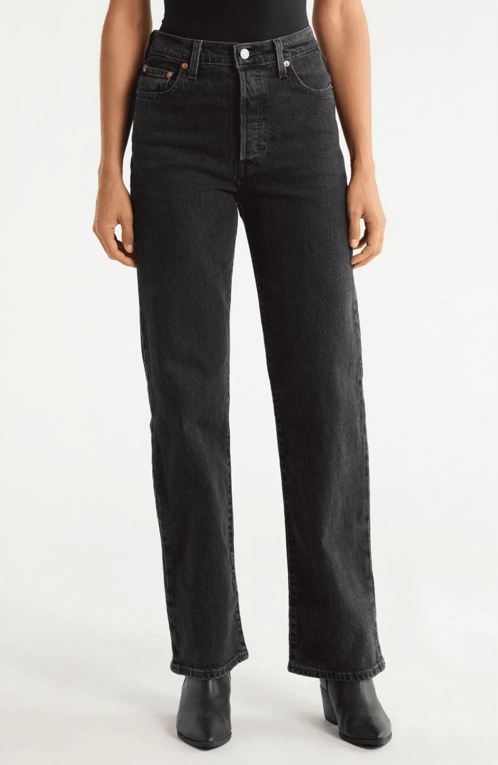 Person in black jeans and boots, hands by sides, white background.