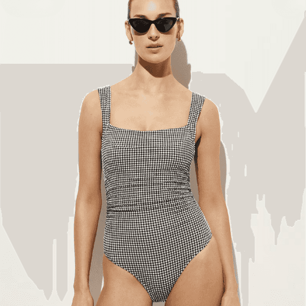 Person in black sunglasses wearing a checkered swimsuit against a plain background.